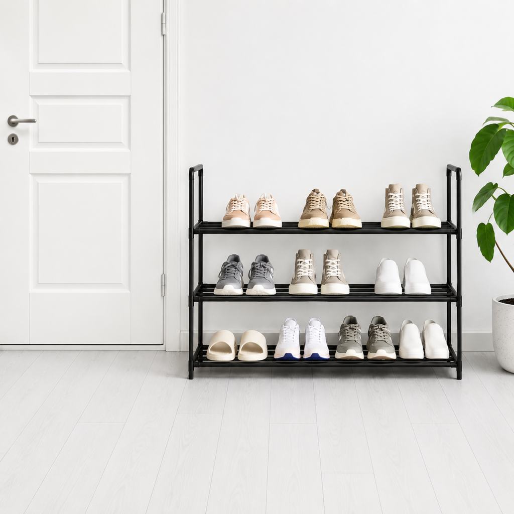A three-tier black metal shoe rack holding various casual shoes and sandals, positioned in a bright, minimalist room next to a white door and a potted green plant.