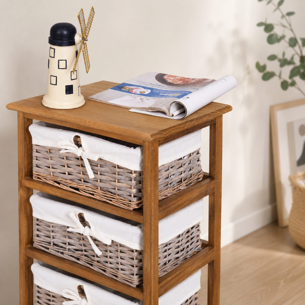A wooden three-tier side table with woven wicker baskets lined with white fabric on each shelf, styled with a small decorative windmill bottle and an open magazine on top, in a softly lit room.