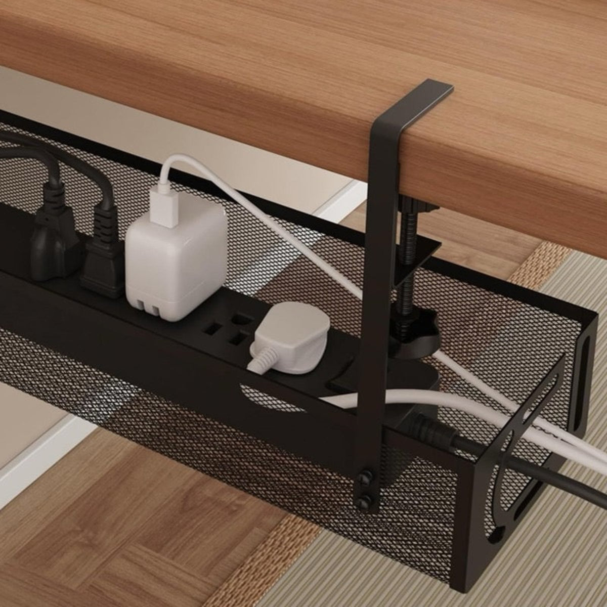 Black mesh cable management tray under a wooden desk, holding power strips and cords, shown in a home office setting.