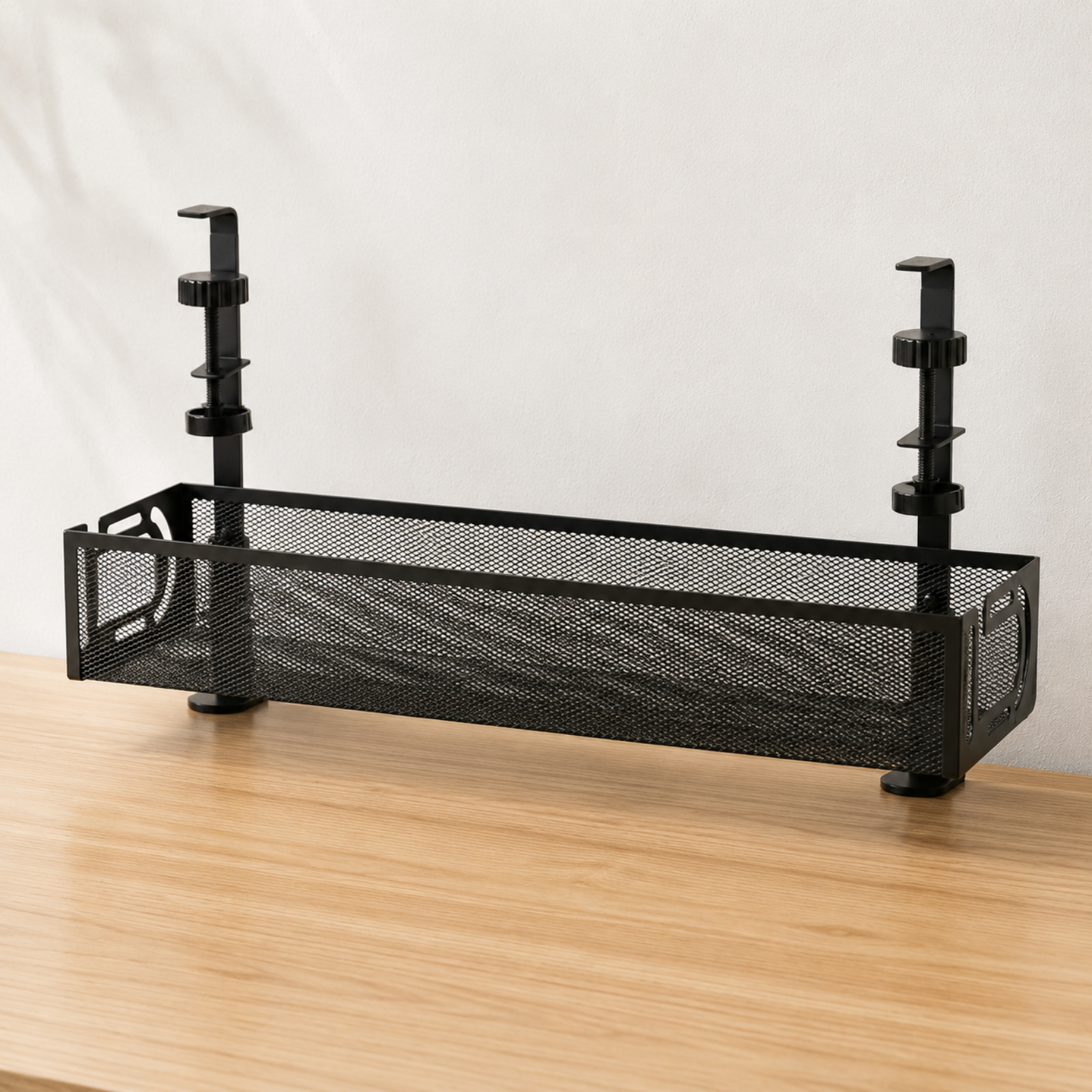 A black metal mesh desk organizer with adjustable vertical supports, shown on a light wood tabletop against a white fabric backdrop.