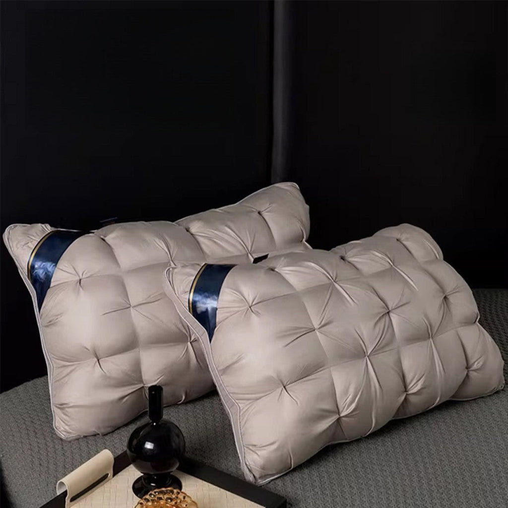 Two quilted rectangular pillows in a light taupe-beige fabric with a dark blue satin band detail, displayed on a textured gray bed against a dark background.