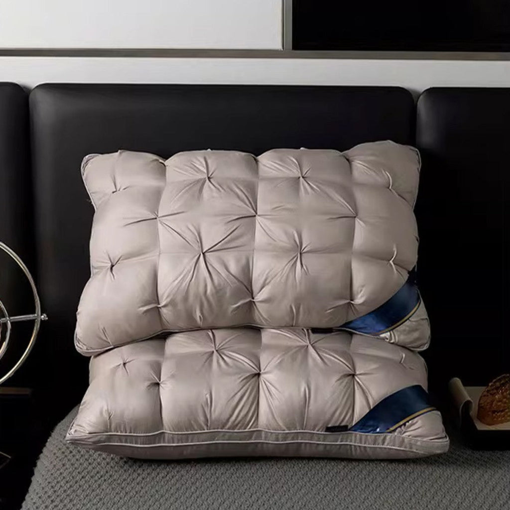 Two stacked rectangular tufted pillows in a light taupe-beige color with a subtle sheen, resting on a gray textured bedspread in front of a black headboard.