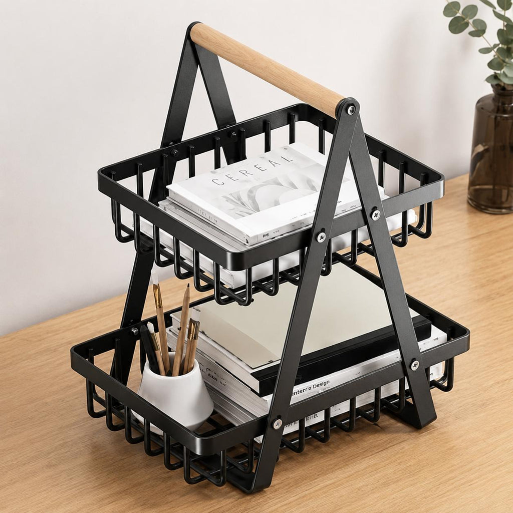 A two-tier black metal desk organizer with a light wood handle, shown on a wooden tabletop with books and a small cup of pens.