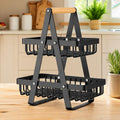 A two-tier black metal wire basket organizer with a wooden handle, shown on a wooden countertop in a kitchen setting.