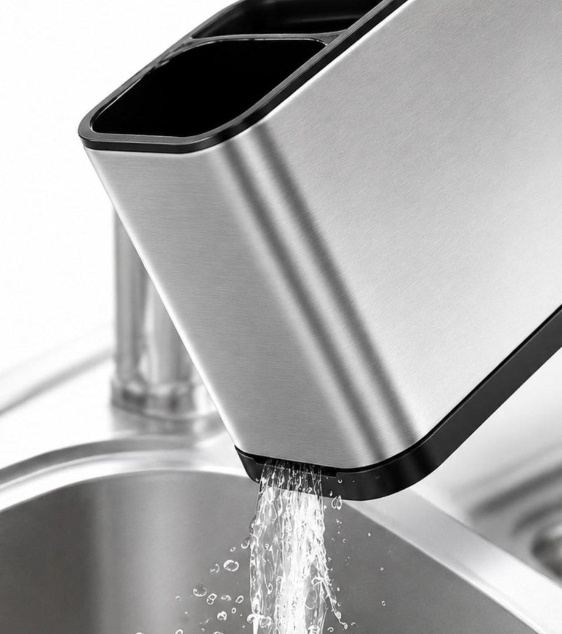 A stainless steel kitchen sink faucet with a rectangular spout pouring water into a matching sink, shown close up against a white background.