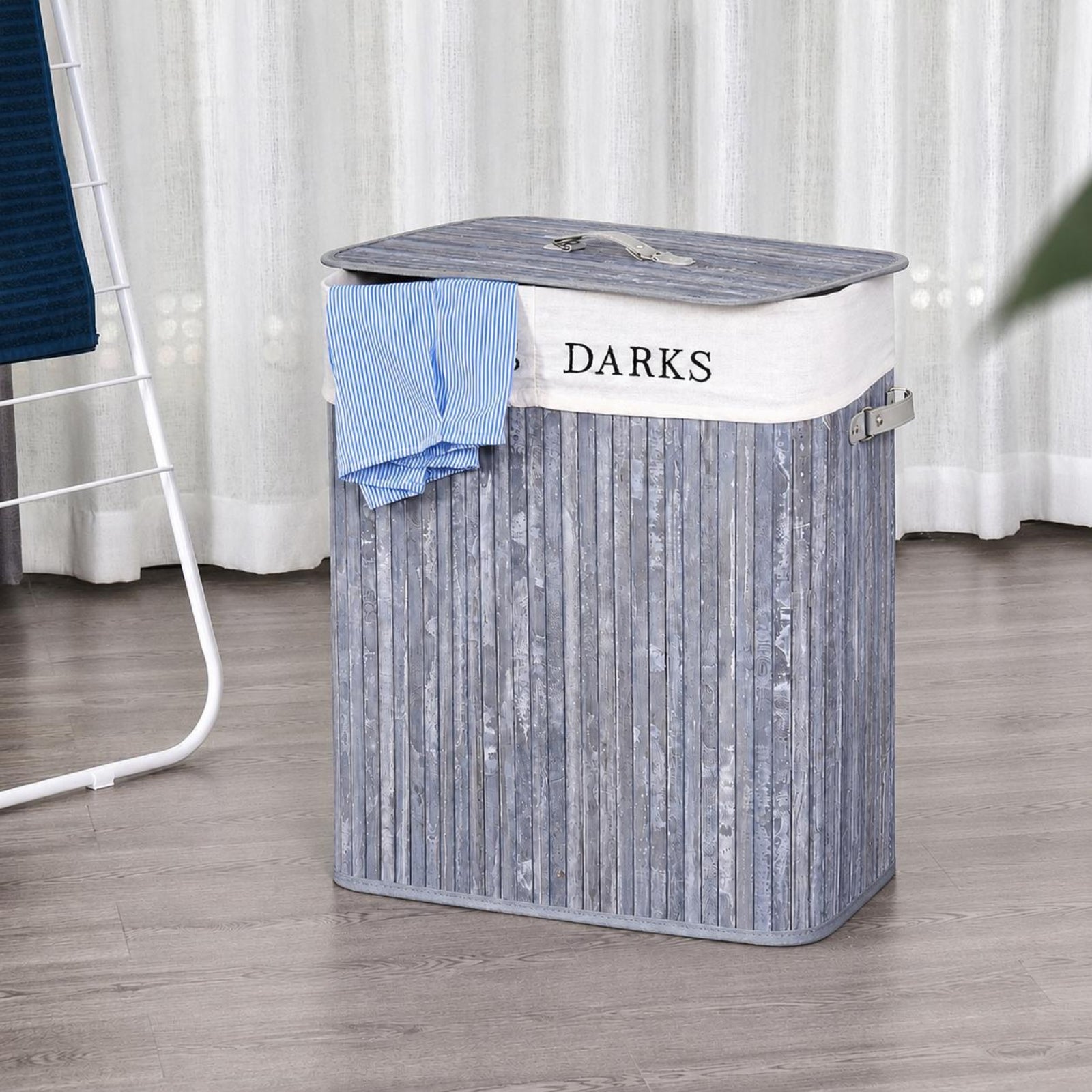 Grey bamboo laundry hamper with white fabric liner labelled Darks, lid with handle, styled on a wood floor with white curtains