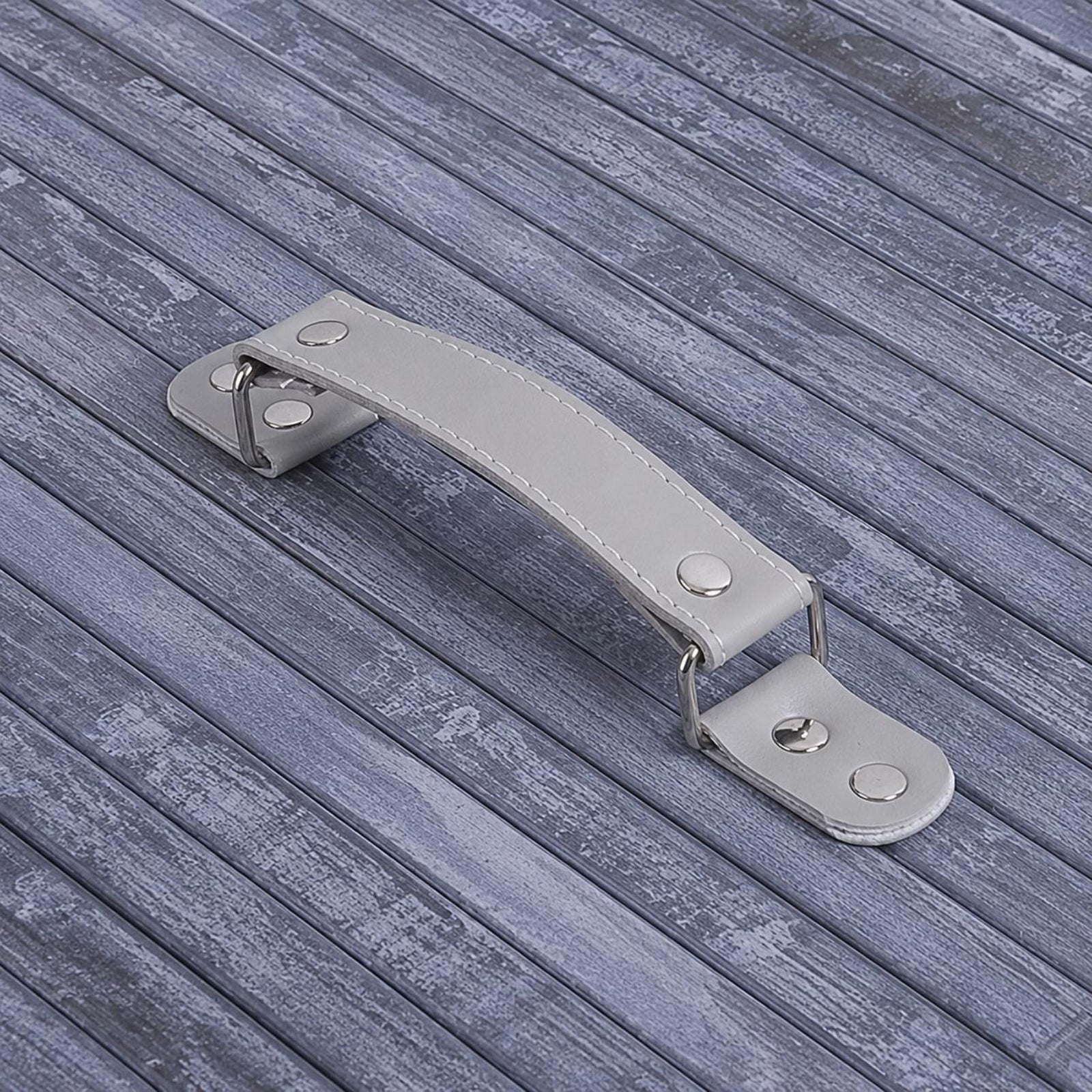 A silver metal and light grey faux-leather door handle with rivets, shown on a grey wood-plank surface.